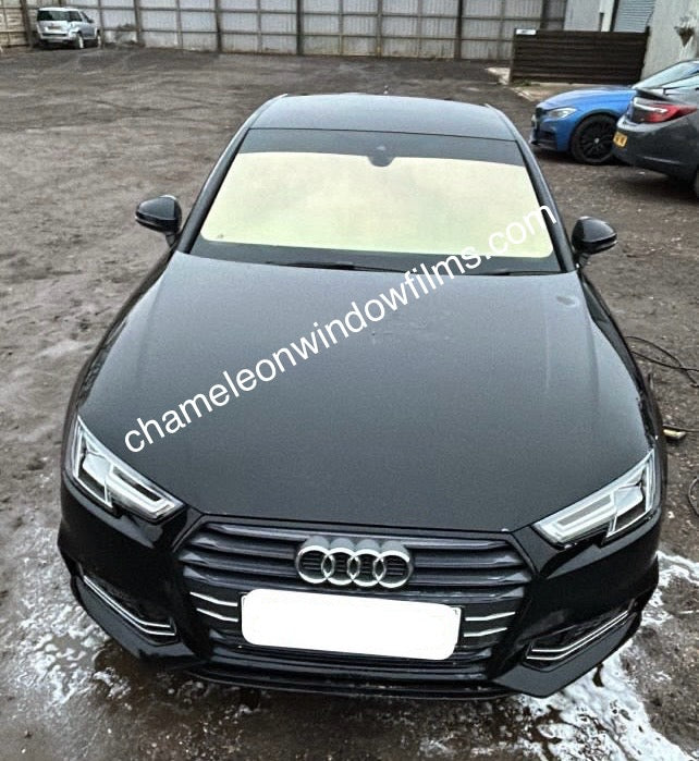 A black Audi car with a yellow/rose gold chameleon window film applied to the front windows, parked in a lot with the branding 'Chameleon Window Films' visible on the image.