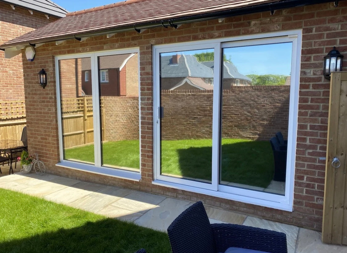 A residential window with silver reflective film applied to it, showing a reflection of an outdoor scene.