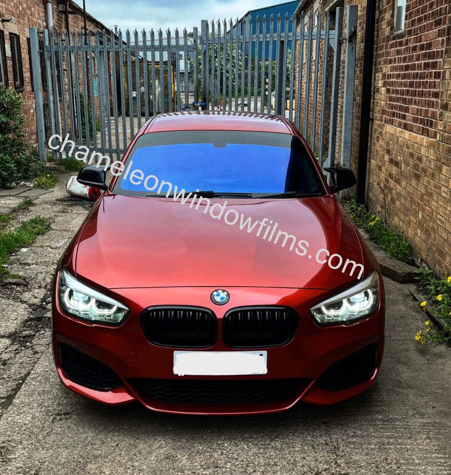 A red car with the Deep Blue Chameleon Window Film applied to its front window, showcasing a chameleon-like appearance under different lighting.
