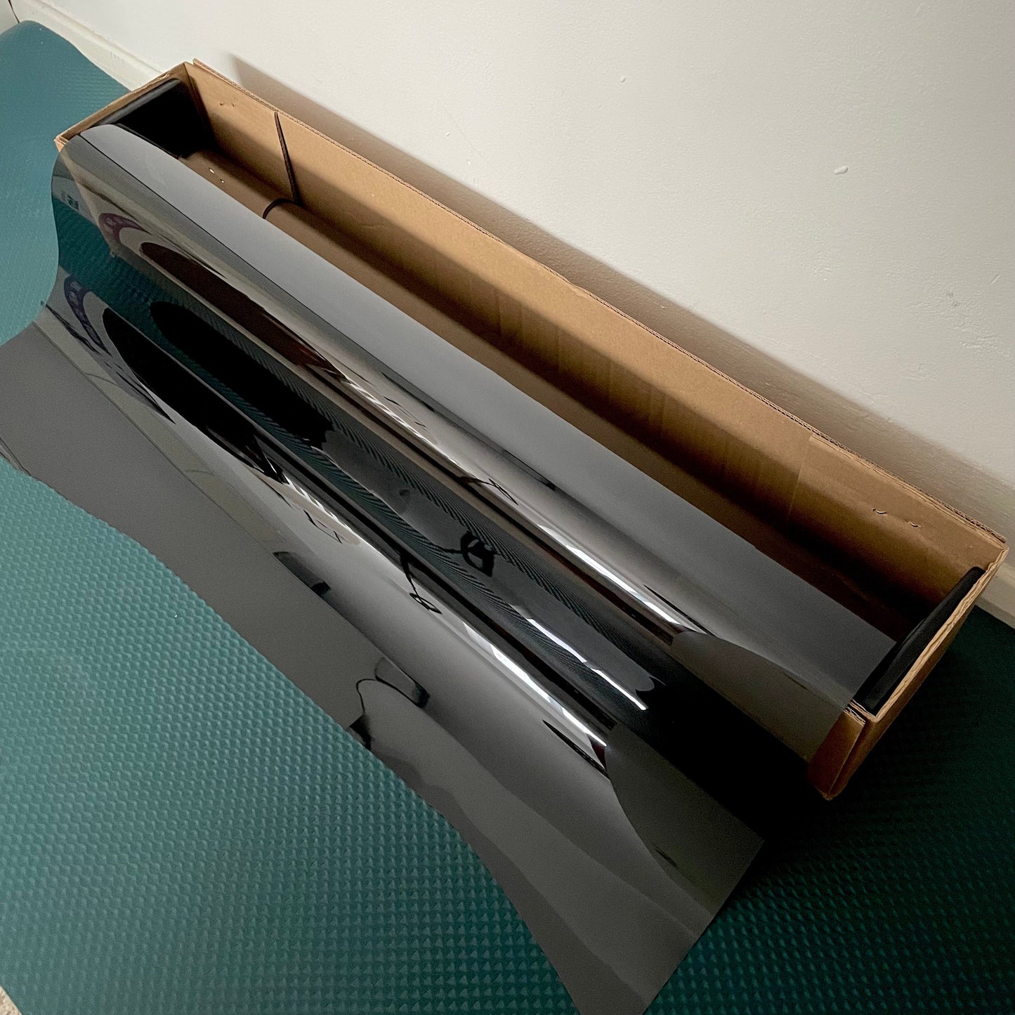 A roll of black automotive nano ceramic window film, displayed unrolled, showing its reflective surface.